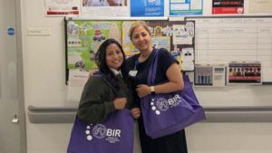 Two colleagues stood together smiling, carrying BARBIR tote bags.